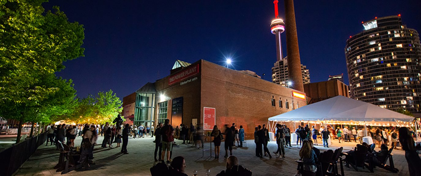 Photo of the Power Plant from outside at night with the CN tower in the background.
