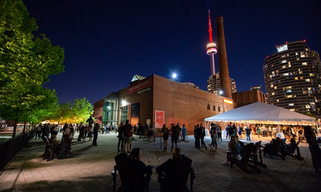 Photo of the Power Plant from outside at night with the CN tower in the background.