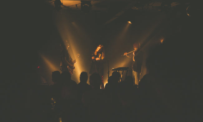 A band is performing on stage in a dark concert venue lit with golden stage lights.