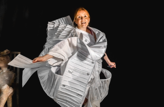 Artist Jenni Juulia dressed in a swirly dress made of white paper with black text on it.