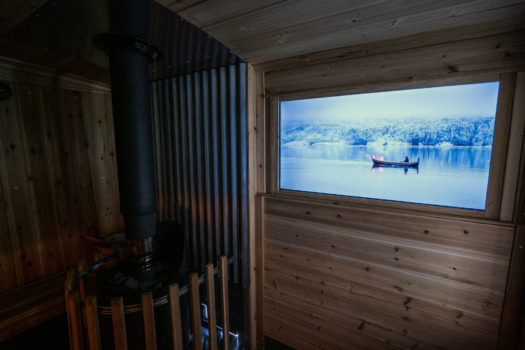 A video of nature playing on a screen inside a wooden sauna in dim lighting.