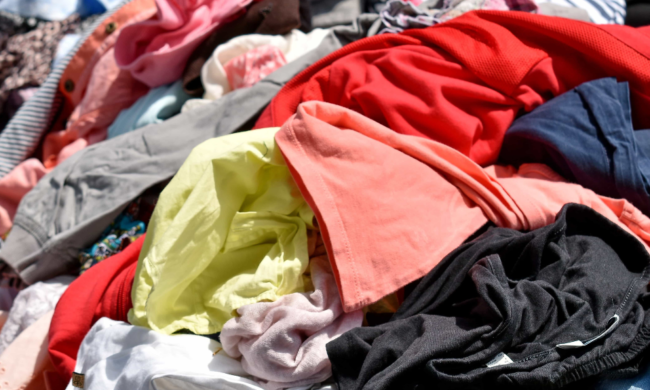 A pile of multi-coloured clothing with the Circular Fashion Festival logo in the bottom left corner.